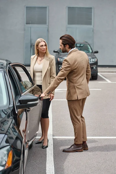 Cropped view of man in formal wear opening rear door of luxury car near elegant businesswoman — Stock Photo