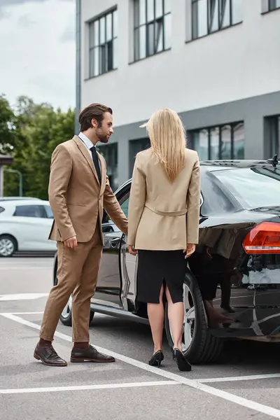 Bearded elegant man opening rear door of luxury car near trendy blonde businesswoman on city street — Stock Photo