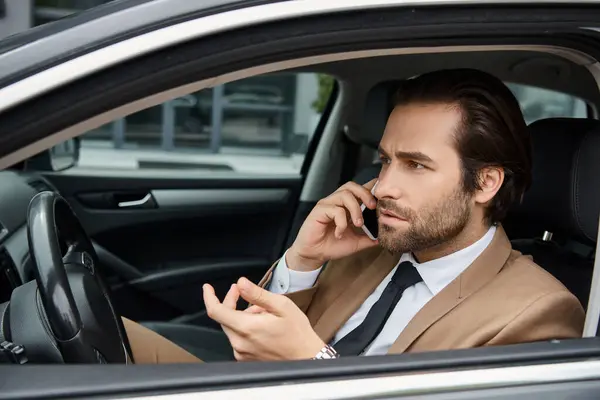 Вдумчивый бизнесмен в бежевом костюме сидит в машине и разговаривает на городской улице, предпринимательство — стоковое фото