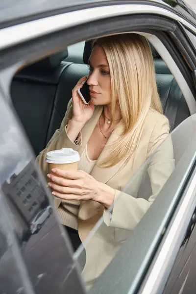 Стильная деловая женщина в формальной одежде сидит с кофе, чтобы пойти и говорить на смартфоне в машине — стоковое фото