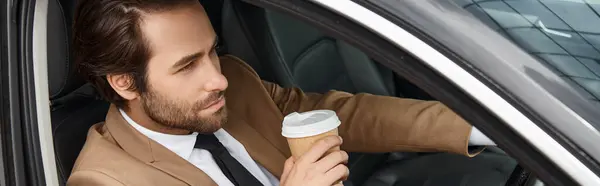 Uomo d'affari barbuto in abito elegante beige che tiene il caffè per andare e guidare auto in strada, banner — Foto stock