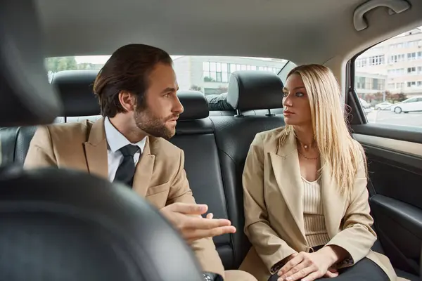 Stylish business couple in formal wear sitting and looking at each other during travel in car — Stock Photo