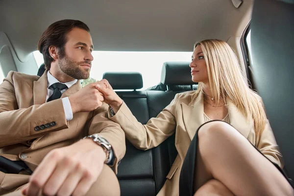 Felice coppia d'affari in abbigliamento formale che si tiene per mano e si guarda durante il viaggio in auto — Foto stock