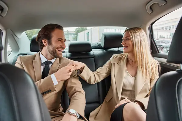 Joyful business couple in formal wear holding hands and looking at each other during travel in car — Stock Photo