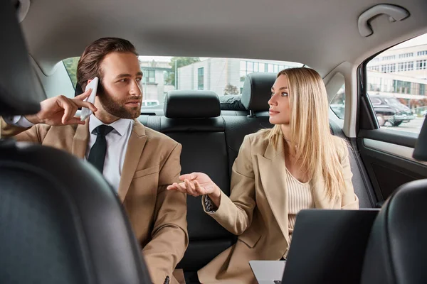 Blonde businesswoman talking to handsome man in formal wear calling on smartphone in luxury car — Stock Photo