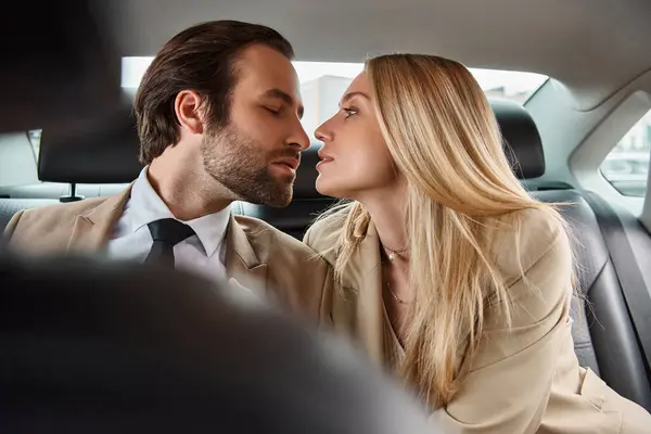 Homme d'affaires élégant et jolie femme blonde assise face à face dans une voiture de luxe, séduction — Photo de stock