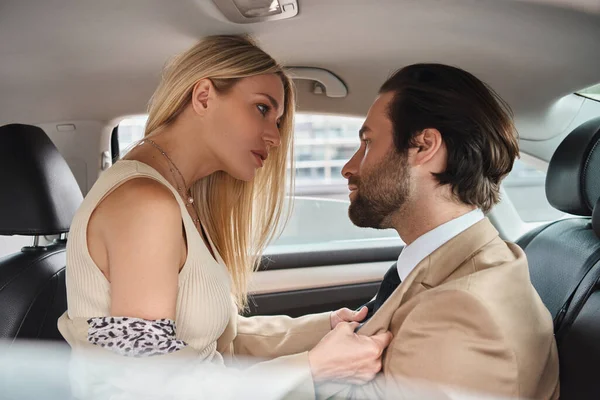 Passionate blonde businesswoman seducing handsome elegant business partner while traveling in car — Stock Photo