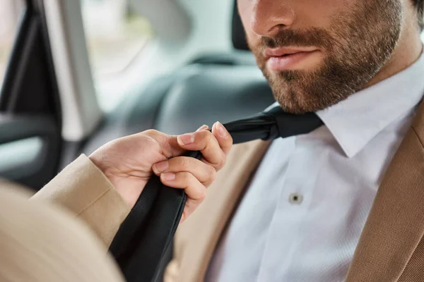 Cropped view of passionate woman pulling tie on bearded business colleague and seducing him in car — Stock Photo