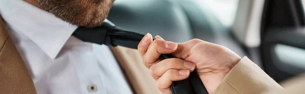 Vue recadrée de femme séduisante tirant cravate sur barbu collègue d'affaires en voiture, bannière horizontale — Photo de stock