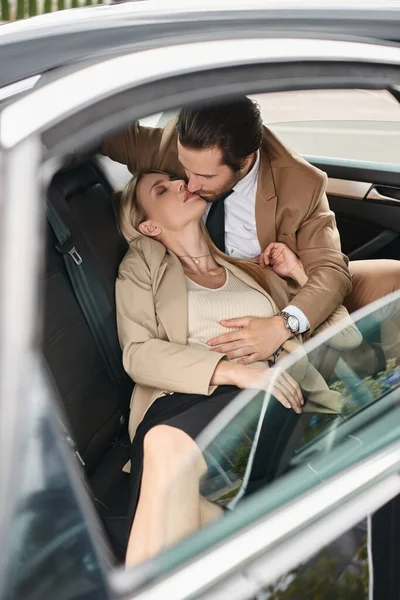 Uomo di tendenza in giacca e cravatta che abbraccia bionda appassionata donna d'affari bianca in viaggio in auto, seduzione — Foto stock