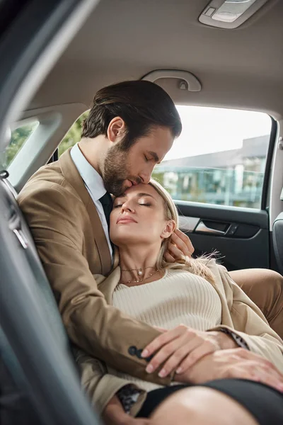 Bell'uomo d'affari con gli occhi chiusi che abbraccia sensuale donna bionda in auto di lusso, storia d'amore — Foto stock