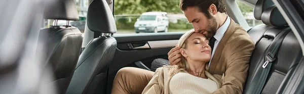 Stylish businessman with closed eyes tenderly embracing sensual blonde woman in luxury car, banner — Stock Photo