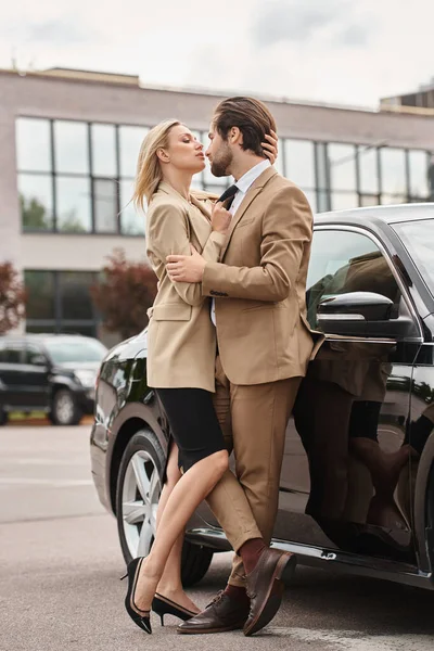 Elegant and passionate business couple in formal wear embracing near car on city street, romance — Stock Photo