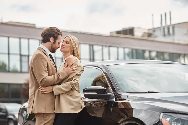 Elegante e apaixonado casal de negócios em desgaste formal abraçando perto do carro na rua da cidade, romance — Fotografia de Stock