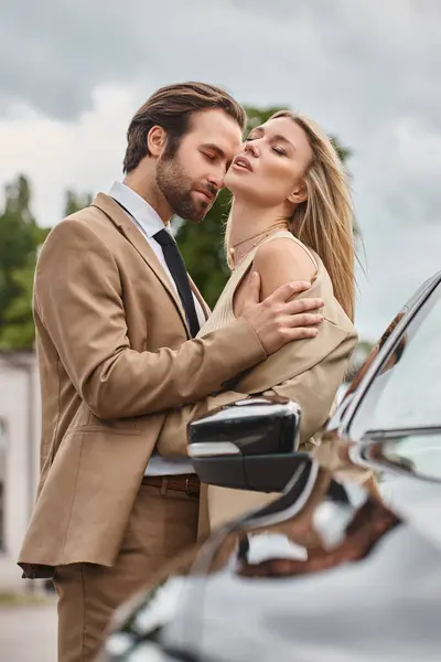 Homme d'affaires en tenue formelle embrassant femme blonde passionnée près de la voiture dans la rue urbaine, passion — Photo de stock
