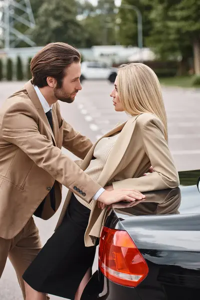 Homme élégant en tenue formelle regardant sensuelle femme d'affaires blonde près de la voiture dans la rue, attraction — Photo de stock