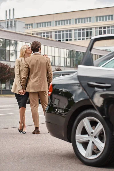 Stylish business couple in formal wear holding hands while standing near car on street, affection — Stock Photo