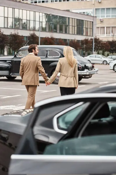 Stylish business couple in formal wear holding hands while walking on car parking, romance — Stock Photo