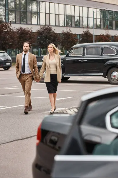 Elegant business couple in formal wear holding hands while walking along car parking, love affair — Stock Photo