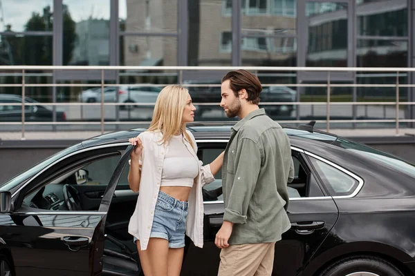 Blonde Frau und bärtiger Mann in stylischer Freizeitkleidung, die sich in der Nähe des Autos anschauen, Attraktion — Stockfoto