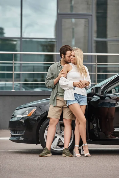 Couple à la mode en vêtements décontractés embrassant près de voiture moderne sur la rue urbaine, romantique datant — Photo de stock