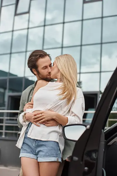 Elegante homem bonito abraçando e beijando namorada loira perto de carro moderno na rua urbana — Fotografia de Stock