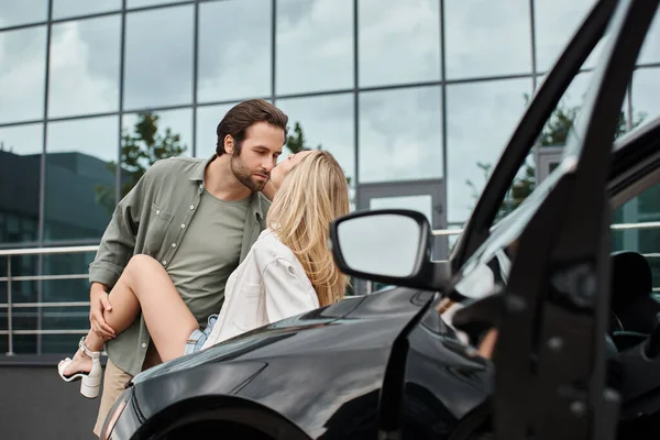 Homme barbu tendance et beau en vêtements décontractés séduire femme blonde près de la voiture dans la rue urbaine — Photo de stock