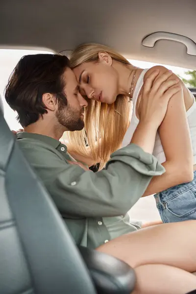 Trendy and passionate blonde woman seducing man on drivers seat in modern car, urban romance — Stock Photo
