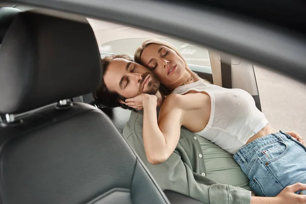 Страстная и стильная пара, обнимающаяся с закрытыми глазами на водительское сиденье в современном автомобиле, любовный роман — стоковое фото