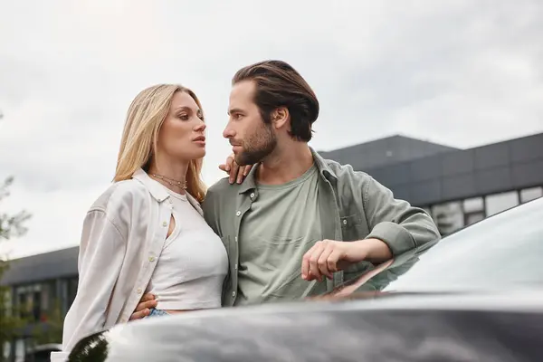 Elegante casal moderno abraçando e olhando uns para os outros perto do carro na rua da cidade, história de amor — Fotografia de Stock