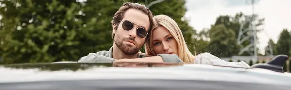 Красивый мужчина в солнечных очках и чувственная блондинка, смотрящая на камеру возле машины на улице, баннер — стоковое фото