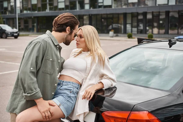 Homme en vêtements décontractés à la mode et lunettes de soleil séduire femme blonde passionnée près de la voiture dans la rue — Photo de stock