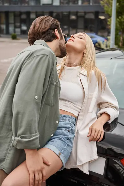 Homme en vêtements décontractés élégants et lunettes de soleil séduisant femme blonde sensuelle près de la voiture dans la rue — Photo de stock