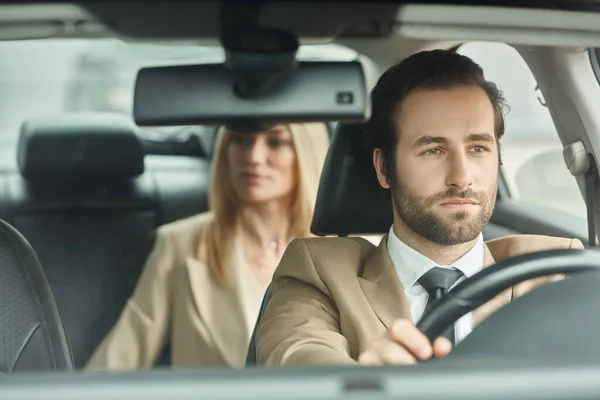 Bel homme élégant dans l'usure formelle voiture de conduite avec femme d'affaires blonde sur le siège arrière — Photo de stock