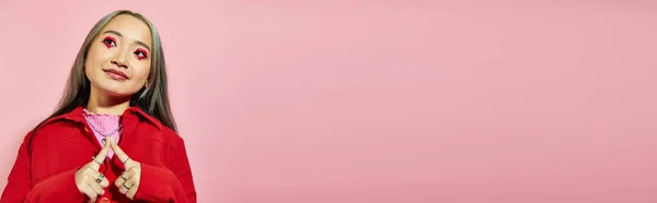 Complacido joven asiática mujer con corazón en forma de ojo maquillaje sonriendo y mirando hacia otro lado en rosa, pancarta - foto de stock