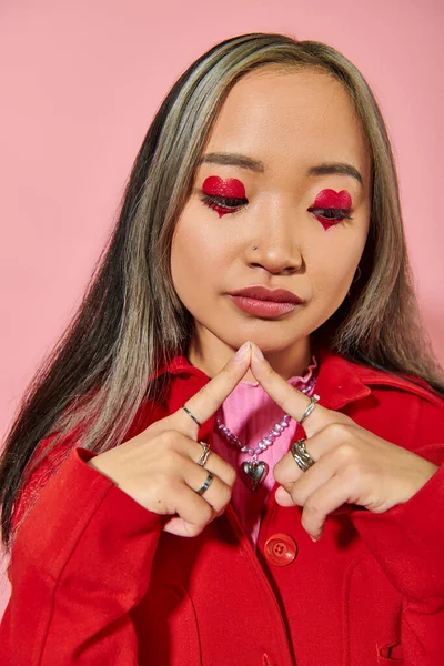 Pensoso giovane asiatico donna con cuore a forma di occhio trucco e tinto capelli guardando giù su sfondo rosa — Foto stock