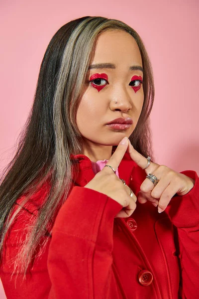 Pensive young asian woman with heart shaped eye makeup and dyed hair looking at camera on pink — Stock Photo