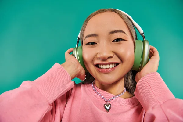 Jolly and young asian woman in wireless headphones listening music on turquoise background — Stock Photo