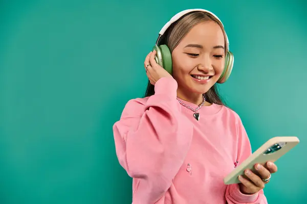 Lustige asiatische Mädchen in drahtlosen Kopfhörern Musik hören und mit Smartphone auf türkis — Stockfoto