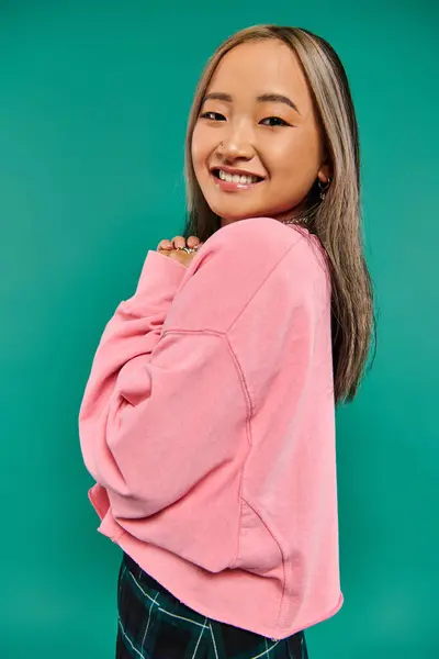Портрет позитивної і молодої азіатської дівчини в рожевому светрі позує на бірюзовому фоні — стокове фото