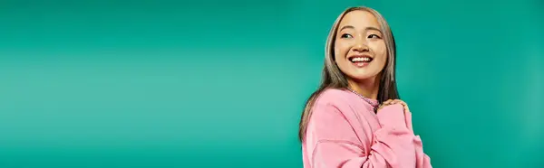 Portrait of cheerful and young asian girl in pink sweatshirt posing on turquoise background, banner — Stock Photo