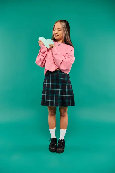 Happy Valentines day, cheerful asian girl holding heart shaped carton on turquoise background — Stock Photo