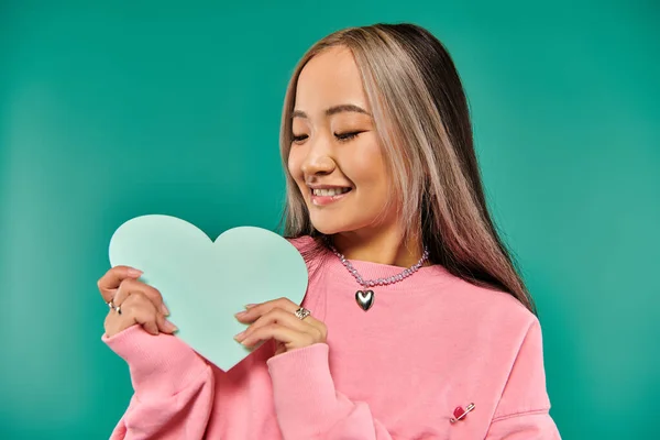 14 febrero concepto, alegre mujer asiática sosteniendo corazón en forma de cartón sobre fondo turquesa - foto de stock