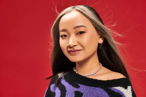 Happy and young asian woman with dyed hair in vibrant sweater with animal print posing on red — Stock Photo