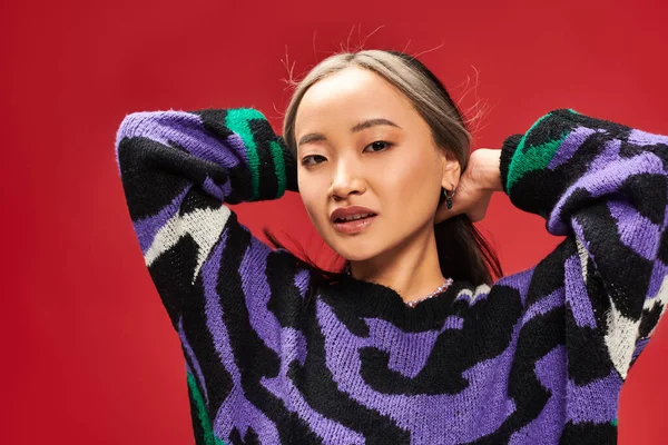 Pretty and young asian woman with dyed hair in vibrant sweater with animal print posing on red — Stock Photo