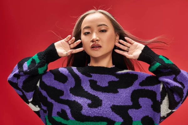Hübsche junge asiatische Frau mit gefärbten Haaren im Pullover mit Animal Print posiert mit den Händen in der Nähe des Gesichts — Stockfoto