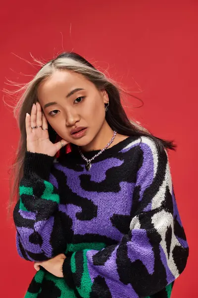 Verführerische junge Asiatin mit gefärbten Haaren im Pullover mit Animal Print posiert mit händennahem Gesicht — Stockfoto