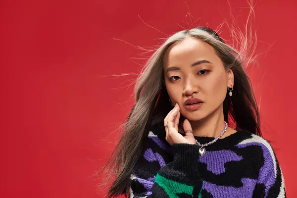 Verführerische junge asiatische Frau mit gefärbten Haaren im Pullover mit Animal Print, die rote Wange berührt — Stockfoto