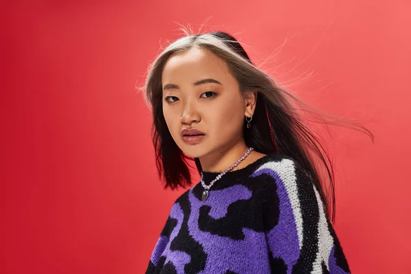 Beautiful young asian model in vibrant sweater with animal print with heart shaped necklace on red — Stock Photo