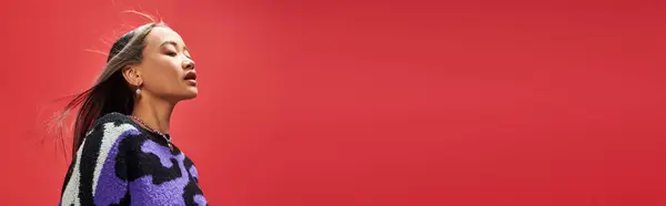 Гарна азіатська дівчина в яскравому светрі з тваринним принтом з кольє у формі серця на червоному, банер — стокове фото